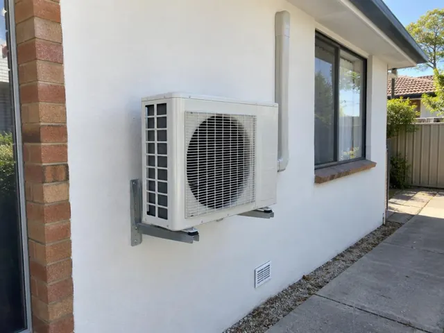 Wall-mounted outdoor air conditioner beside a window on a white rendered house in Greenwith